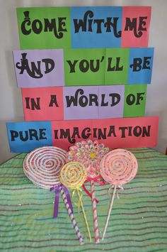 some lollipops are sitting on a bed with colorful signs behind them that say come with me and you'll be in a world of pure imagination