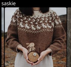 a woman wearing a brown and white sweater holding a small wooden object in her hands