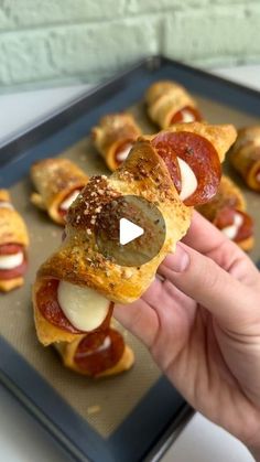 a person is holding up some food on a baking sheet with pepperoni and cheese