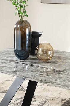 a marble table with two vases and a plant on the top, in front of it