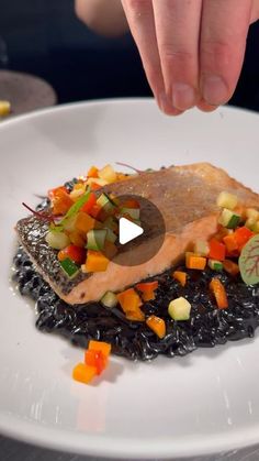 a person reaching for a piece of fish on top of black rice with carrots and cucumbers