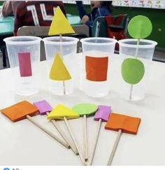 plastic cups with different colored shapes and sticks sticking out of them, sitting on a table