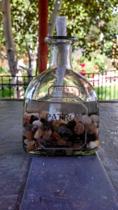 a bottle filled with rocks sitting on top of a cement slab next to trees and bushes