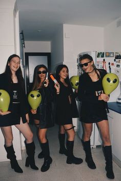 four women in black dresses holding balloons and smiling at the camera while standing in a kitchen