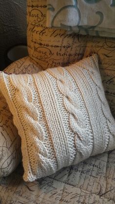 two knitted pillows sitting on top of a bed next to a pillow with the word love written on it