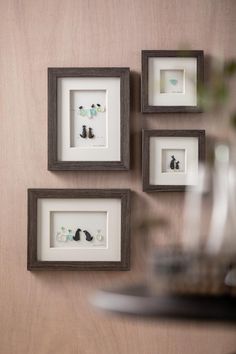 four framed pictures hang on the wall above a vase with flowers and other items in it