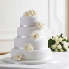 a three tiered white wedding cake with flowers on the top and bottom, sitting on a table