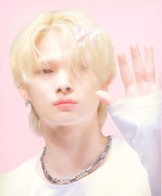 a man with blonde hair wearing a white shirt and silver necklace holding his hand up to the side