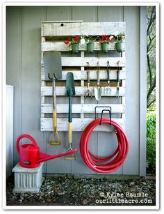 a garden tool rack with gardening tools hanging on it's side wall next to a fire hydrant