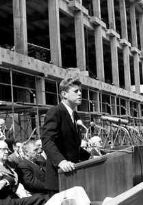 a man standing at a podium in front of a group of men sitting next to each other