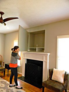 a woman standing in a living room next to a fire place and a ceiling fan