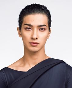 a young man with black hair wearing a dark shirt and posing for the camera in front of a white background