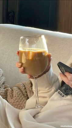 a woman sitting on a couch holding a glass of wine and a cell phone in her hand