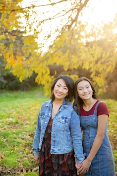 two young women standing next to each other in front of a tree with yellow leaves