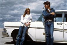 a man and woman standing next to a white car in front of a cloudy sky