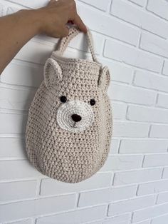 a crocheted bear bag hanging on a brick wall with a hand holding it