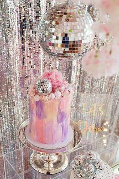 a pink and purple cake sitting on top of a table next to a disco ball