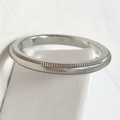 a white gold wedding band with beaded edges on a plain surface, ready to be worn