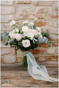 a bouquet of white flowers sitting on top of a table next to a brick wall