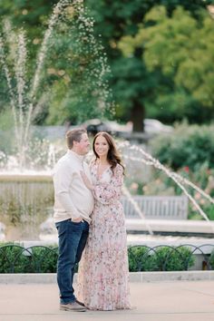 an engaged couple standing in front of a fountain