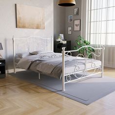 a white bed sitting on top of a hard wood floor next to a lamp and window