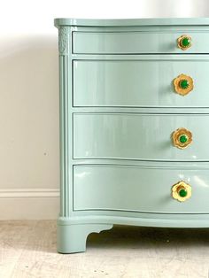 a blue dresser with green knobs on it's drawers and gold handles, against a white wall