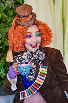 a woman with red hair and makeup is dressed as a mad clown holding a cup