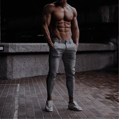 a shirtless man is standing on a brick walkway and posing for the camera with his hands in his pockets