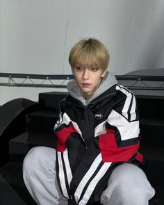 a young man sitting on top of a black and white bench with his hands in his pockets