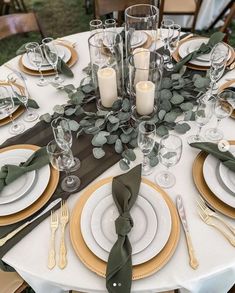 the table is set with white and gold plates, silverware, greenery and candles