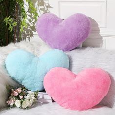 two heart shaped pillows sitting on top of a white fur covered bed next to flowers