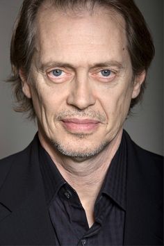 a close up of a person wearing a black shirt and suit with his eyes wide open