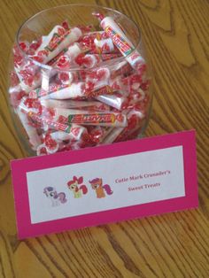 a glass bowl filled with candy next to a pink label on a wooden table top