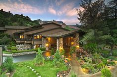 a large house with lots of trees and plants in front of it at night time