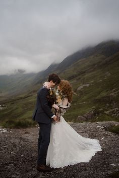 a bride and groom standing on top of a mountain with their arms around each other