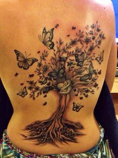 the back of a woman's body with butterflies on it and a tree in the middle