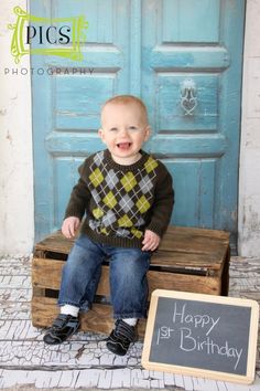 a baby sitting on a wooden crate in front of a blue door with a happy 1st birthday sign