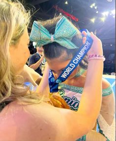 a woman holding onto a blue ribbon with a bow on it's head in front of a crowd