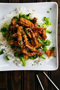 chicken and broccoli served over rice on a plate with chopsticks next to it