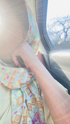 a woman wearing a colorful scarf sitting in a car with the sun shining behind her