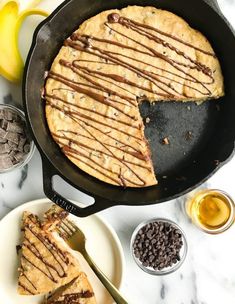 a skillet cake with chocolate drizzled on top and bananas in the background