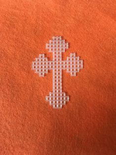 the cross is made out of plastic beads on an orange shirt with white stitching