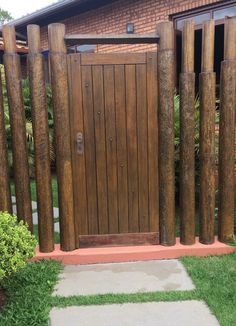 a wooden gate in front of a brick building with green grass and bushes around it