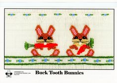 two bunny rabbits sitting on top of a white table cloth with blue and green trim