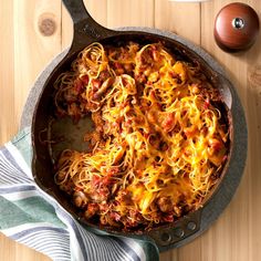 a skillet filled with spaghetti and meat on top of a wooden table next to an egg