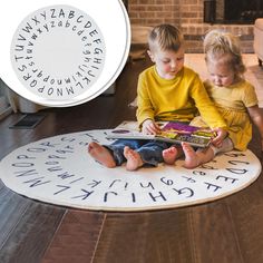 two children sitting on the floor reading a book with letters and numbers written in it