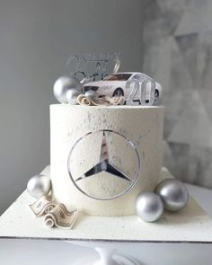 a birthday cake decorated with silver balls and mercedes logo on top is sitting on a table