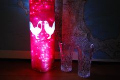 two vases and one glass are lit up in the dark with pink lights on them