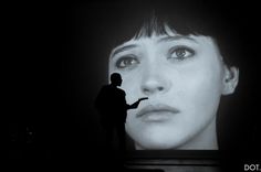 a man standing in front of a large screen with a woman's face on it