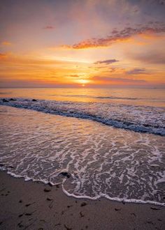 the sun is setting over the ocean with footprints in the sand and waves coming ashore